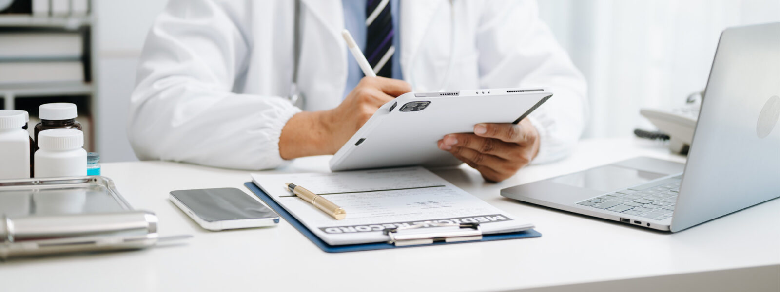 doctor on work-issued tablet consults his patient's medical record on paper and on his work-issued computer