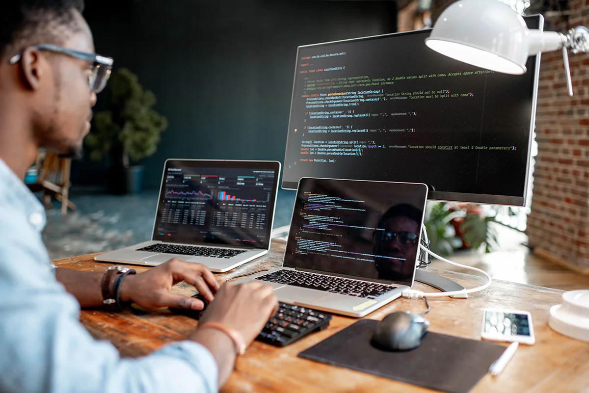 An office employee sits at a desk in front of three computers, showing the concept of IT security for businesses