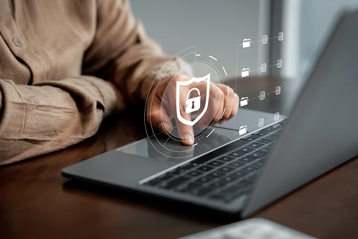 An office worker sitting at their desk in front of a laptop, with an overlay illustration of a padlock, showing the concept of IT security