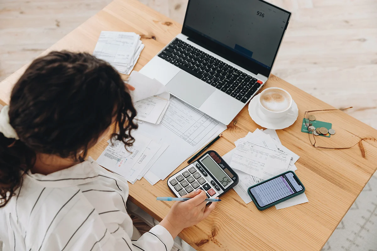 An overhead view of a small business owner doing calculations at a desk with papers and a laptop, showing the concept of IT budgeting strategies