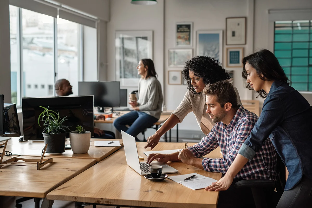 A team of employees working at a small business gather around a laptop in an office, showing the concept of IT pain points that small businesses face